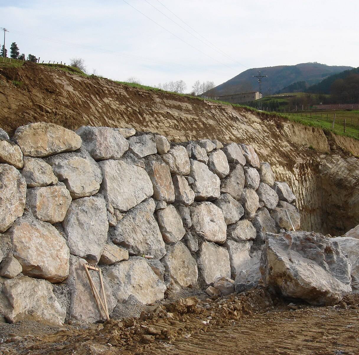 Large rock retaining wall being built against a cut slope
