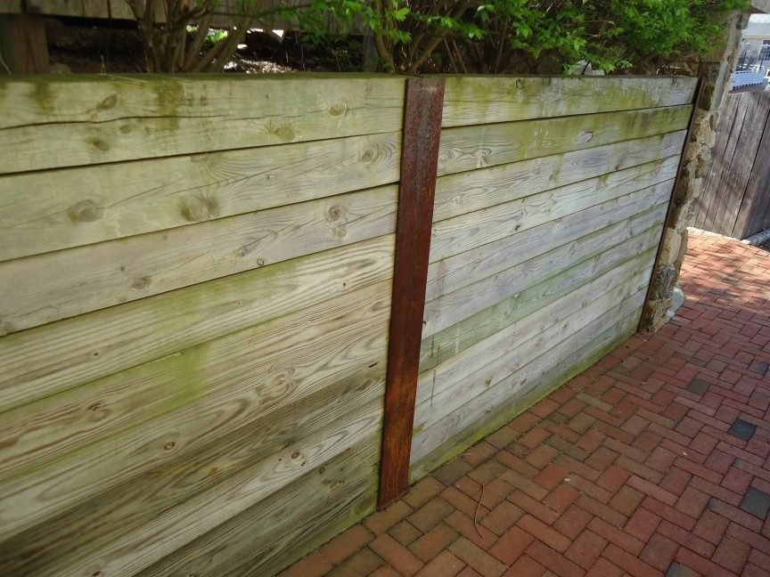 Timber sleeper retaining wall held by steel posts beside a brick path